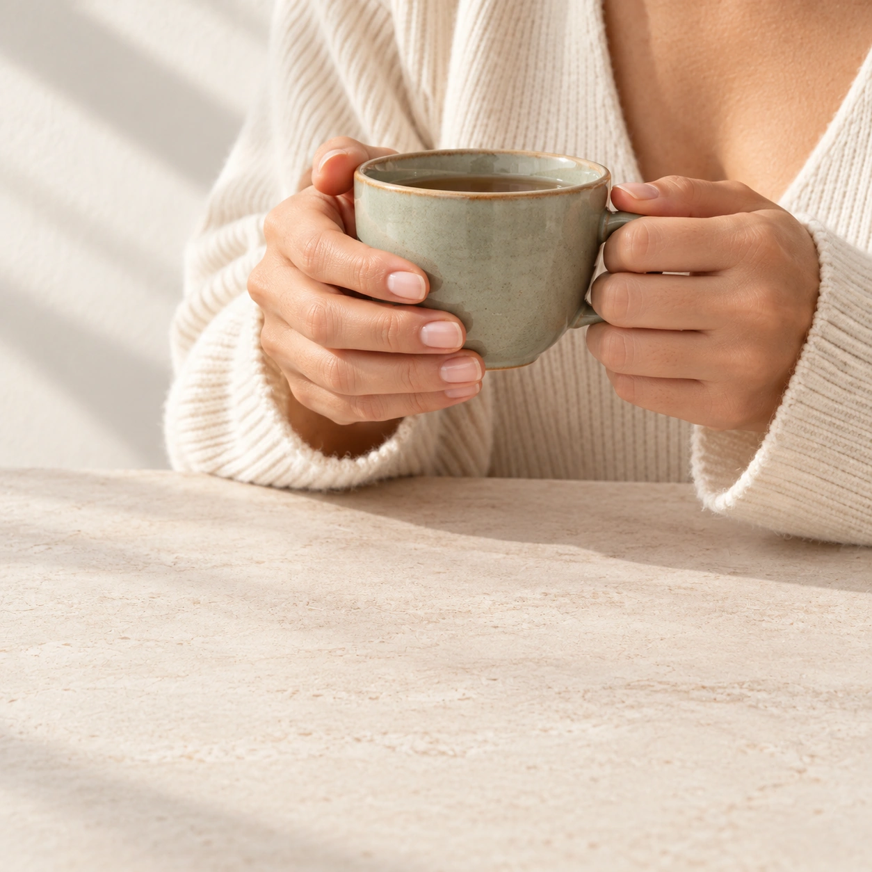 Hände halten eine Keramiktasse über einem hellen Steintisch